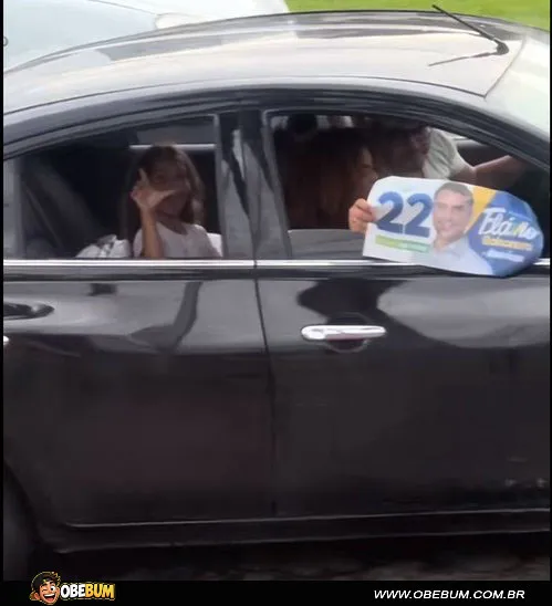 Carro com material de campanha de Flávio Bolsonaro e menina no banco de trás fazendo um gesto com a mão.